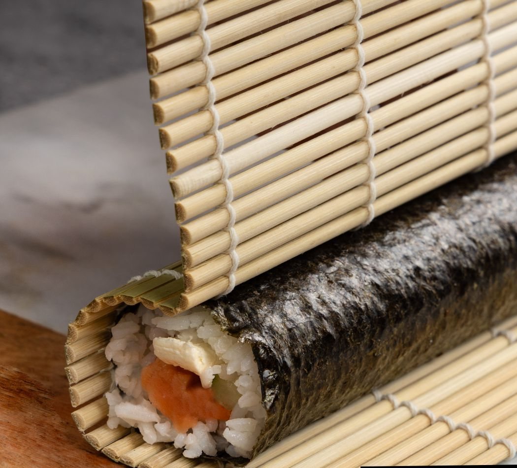 A maki roll being shaped on a bamboo mat