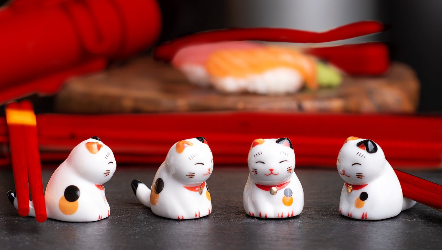 Four lucky-cat chopstick rests with red chopsticks and sushi