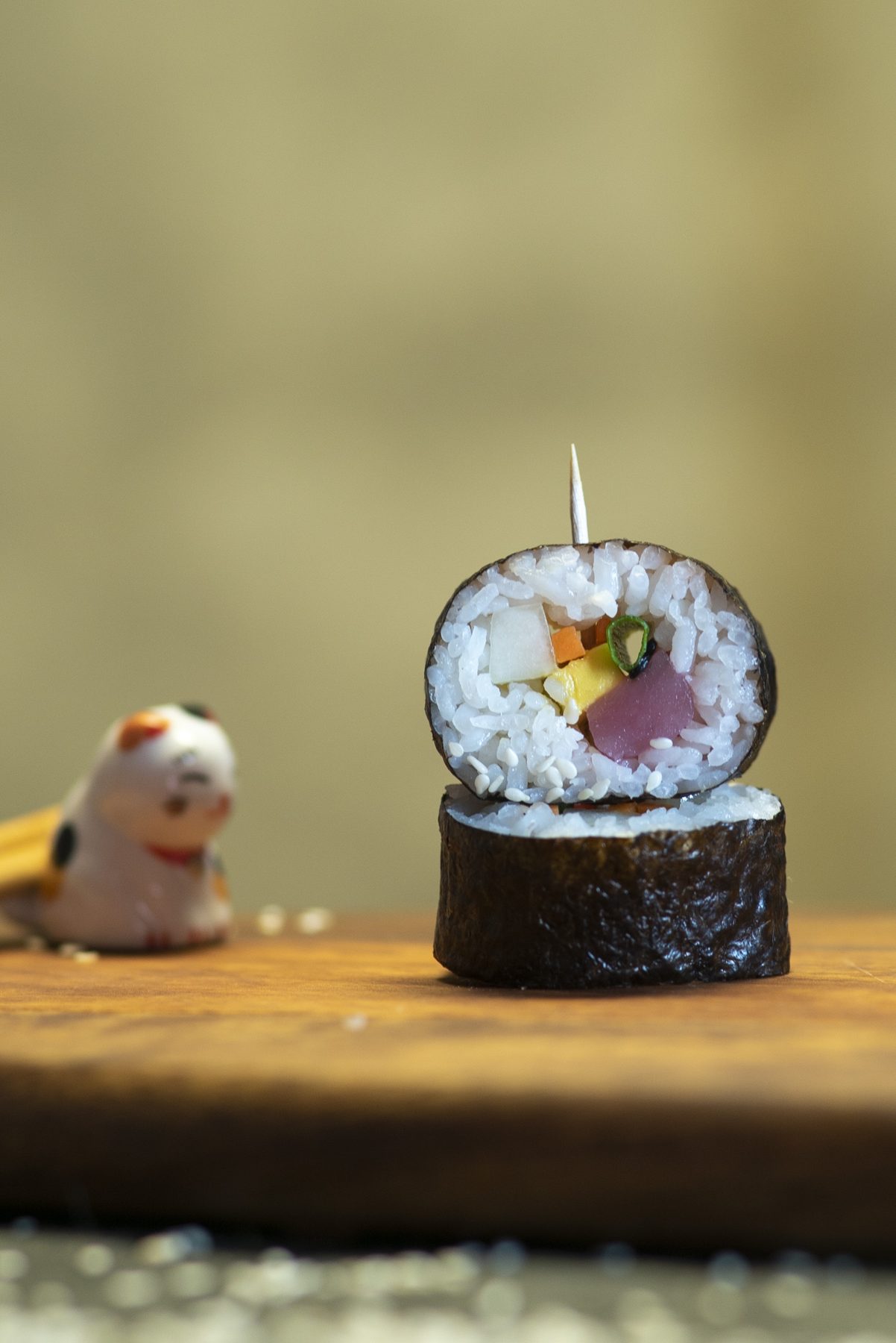 A lucky-cat chopstick rest beside a single maki roll
