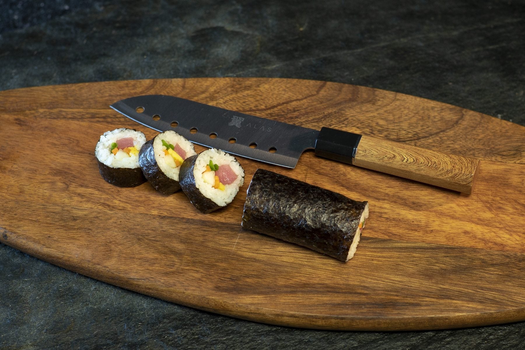 Finished maki rolls next to the sushi knife on a wooden board